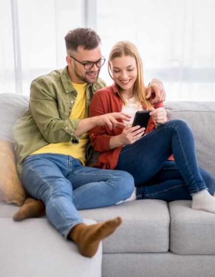 A couple sitting on a couch looking at a cellphone.